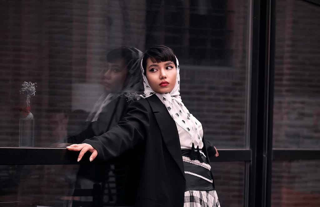 A Woman Wearing a Headscarf and a Blazer Leaning on a Glass Panel