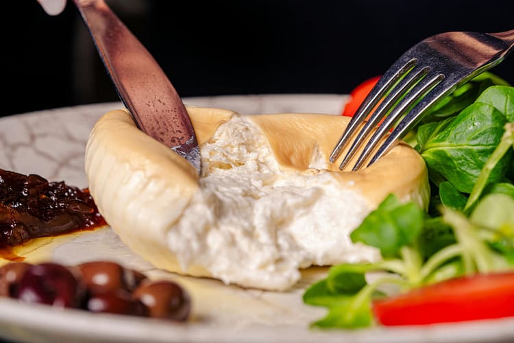 Close-up of creamy cheese served with salad greens, olives, and sundried tomatoes.